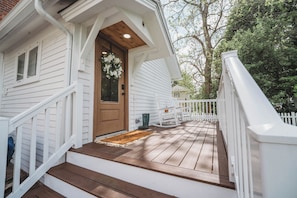 Una casa blanca con puerta principal de madera, un porche con barandilla blanca y una escalera de madera que lleva a la puerta.