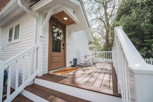 Une maison blanche avec une porte dâentrĂ©e en bois, un porche dotĂ© dâune balustrade blanche et un escalier en bois menant Ă la porte.
