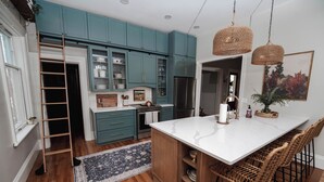 A kitchen with teal cabinets, a white island, wicker chairs, and a ladder. - Charming Restored Historic 3BR Home - The Larrabee (Williamston)
