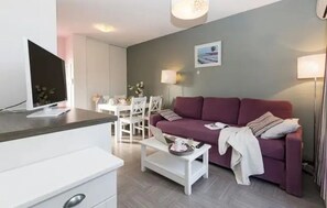 En moderne stue med sofa, sofabord, fjernsyn og et spiseområde med stole og bord.