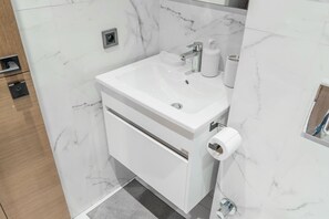 Een moderne badkamer met een wastafel van wit marmer, een spiegel, een zeepdispenser en een toiletrolhouder.