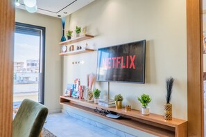 A modern living room with a mounted TV, wooden shelves with decorative items, a sofa, and a window with a view. - Wonderful 1-bedroom apartment with AC in vibrant Casablanca (Casablanca)
