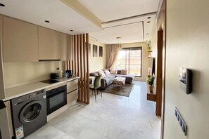 A modern kitchen with a washing machine, a dining area with a sofa and table, and a living room with a sofa and a TV. - Wonderful 1-bedroom apartment with AC in vibrant Casablanca (Casablanca)