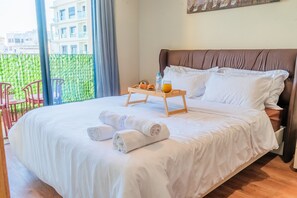 Een net opgemaakt bed met witte lakens, een dienblad met croissants en sap, en een uitzicht op gebouwen door grote ramen.