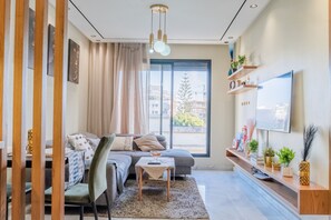 Een moderne woonkamer met een bank, een salontafel, een televisie en een groot raam met uitzicht op gebouwen.
