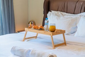 Ein ordentlich bezogenes Bett mit einem Tablett mit Croissants, einer Wasserflasche und einem Glas Orangensaft.