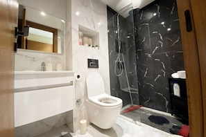 A modern bathroom with a white toilet, a glass shower enclosure, and marble walls. - Wonderful 1-bedroom apartment with AC in vibrant Casablanca (Casablanca)