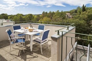 Terraço com mesa e cadeiras, vista para árvores e um prédio ao fundo.