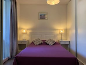 A hotel room with a bed, two bedside tables, and a window with curtains. - Appartement 3 étoiles - Piscine  - ccbgfcd (Gréoux-les-Bains)