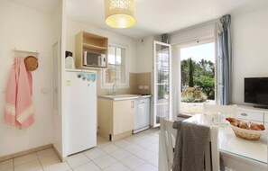 Une cuisine compacte Ă©quipĂ©e dâun rĂ©frigĂ©rateur, dâun four Ă micro-ondes et dâun Ă©vier, un coin repas avec une table et des chaises, et une grande fenĂȘtre donnant sur un paysage verdoyant.