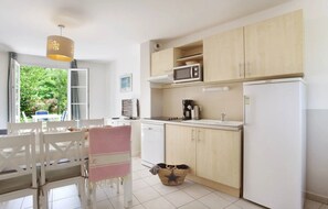 Une cuisine avec des meubles blancs, un four à micro-ondes, une machine à café et un réfrigérateur. On y trouve une table à manger avec des chaises et une fenêtre donnant sur un paysage verdoyant.