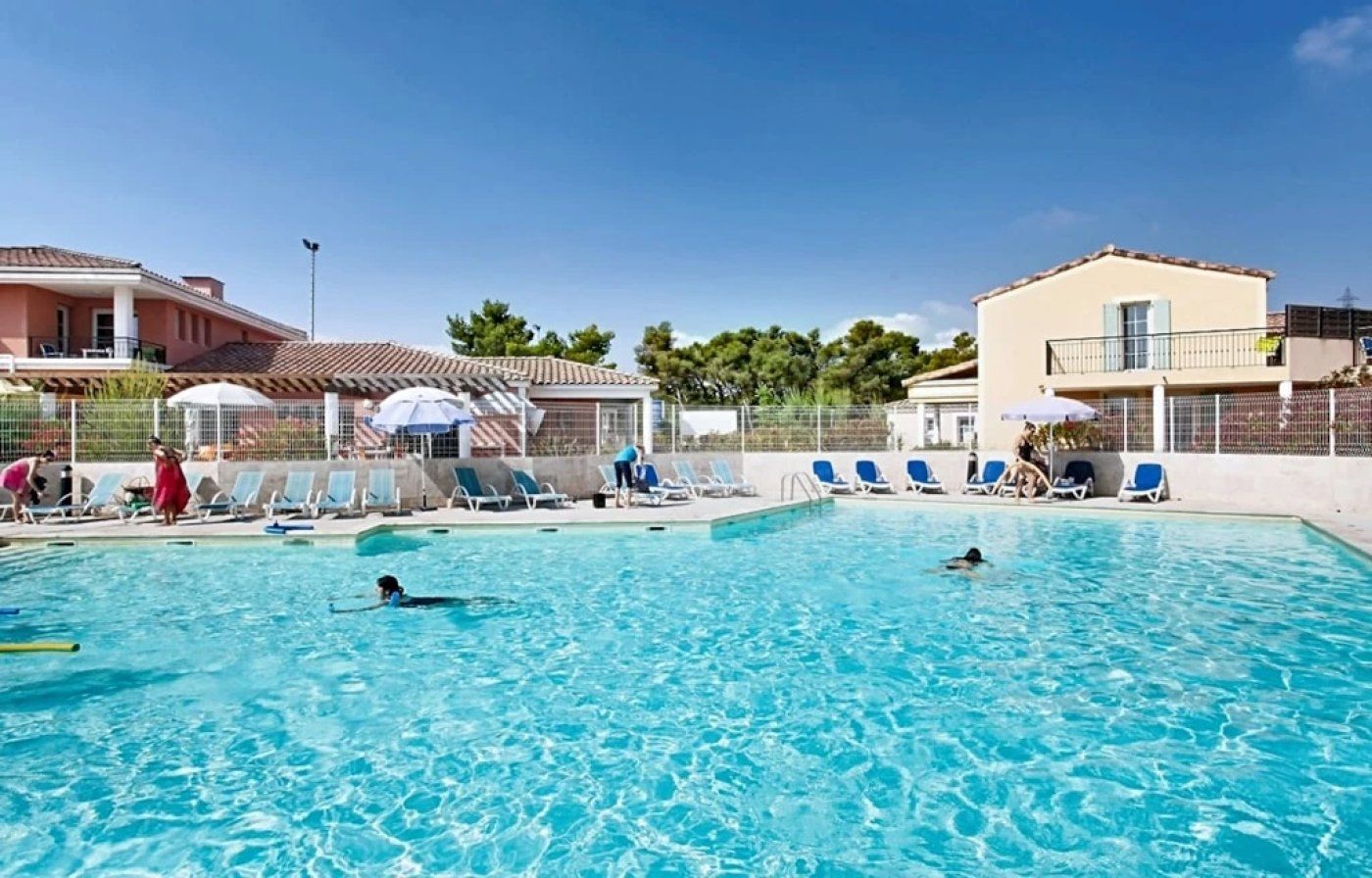 Une piscine entourée de bâtiments, avec des chaises longues et des parasols.
