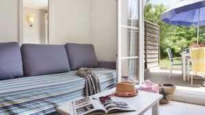 A room with a sofa, a table with a magazine, and a view of the outdoors. - Camping 3 étoiles - ccbgfbi (Cabriès)