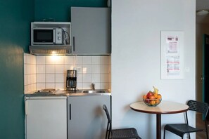 A compact kitchen with a microwave, coffee maker, and a small sink. There is a dining area with a table and chairs, and a bowl of fruit on the table. - Appartement 2 étoiles - ccbgff0 (Brest)