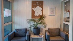 Een receptiezone met twee grijze fauteuils, een tafel met een bloempot, een kaart aan de muur en een raam met uitzicht.