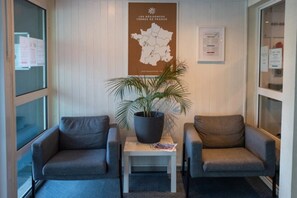 A reception area with two grey armchairs, a table with a potted plant, a map on the wall, and a window with a view. - Appartement 2 étoiles - ccbgff0 (Brest)