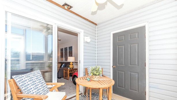 A covered patio with a wooden chair, a small round table, and a grey door. - Rehoboth Perfect 2BR Condo sleeps 6 with a Pool (Rehoboth Beach)