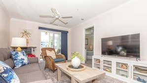 A living room with a sofa, a coffee table, a TV, and a ceiling fan. - Rehoboth Perfect 2BR Condo sleeps 6 with a Pool (Rehoboth Beach)