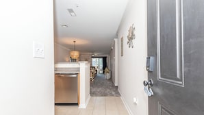 A hallway leading to a kitchen with a dishwasher, a dining area with chairs and a table, and a door with a keyhole. - Rehoboth Perfect 2BR Condo sleeps 6 with a Pool (Rehoboth Beach)