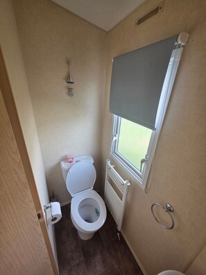 Un baño pequeño con inodoro, radiador, ventana y toallero.