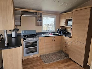 A compact kitchen with a gas stove, oven, and a microwave. - 2-bed Caravan - Sleeps 6 - Pets - Beach Access (Skegness)
