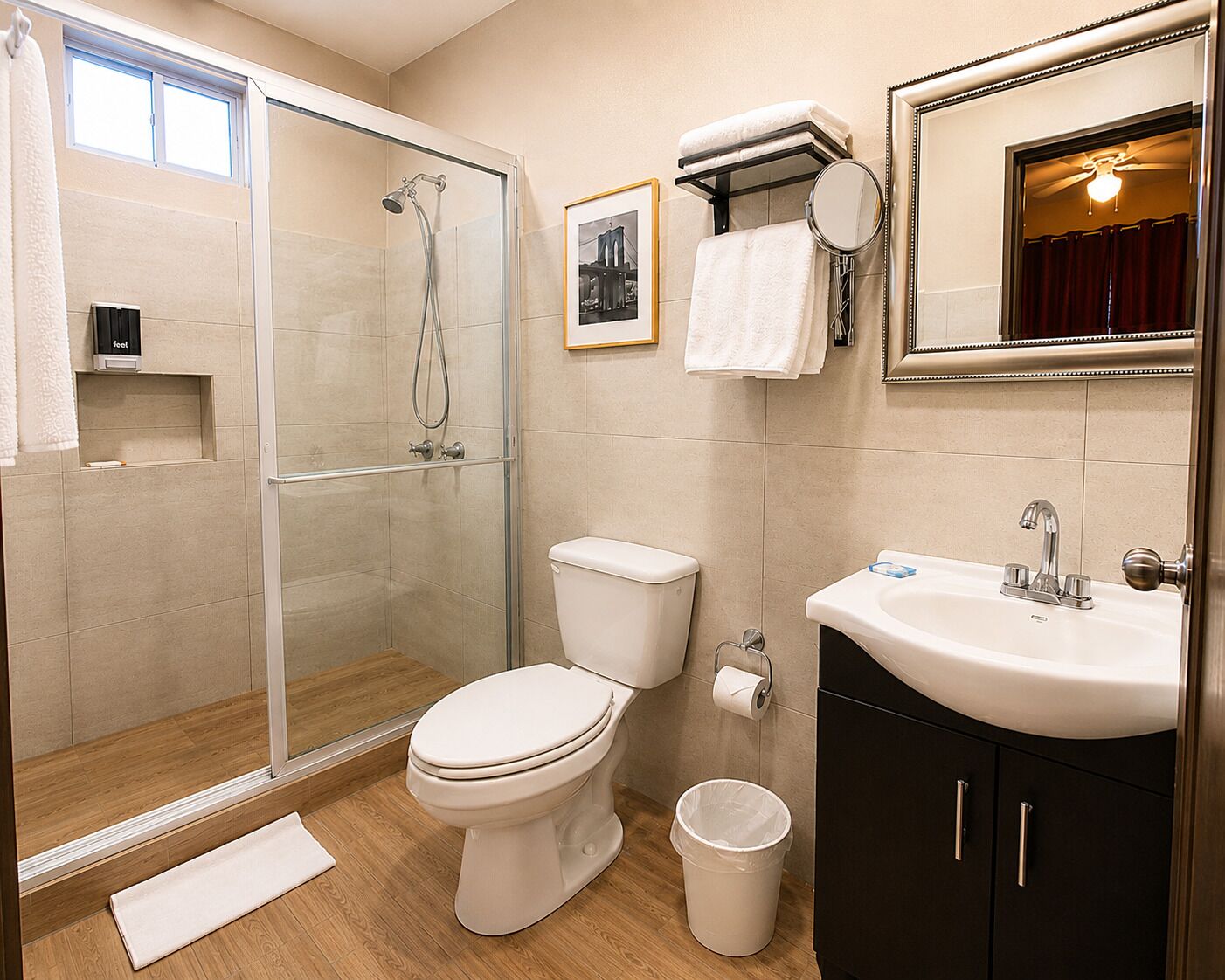 A bathroom with a glass-enclosed shower, a toilet, a sink with a mirror, and a framed picture on the wall.