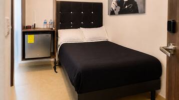 Ein Hotelzimmer mit einem Bett, einem Deckenventilator, einem Gemälde, einer Minibar und einer Tür.
