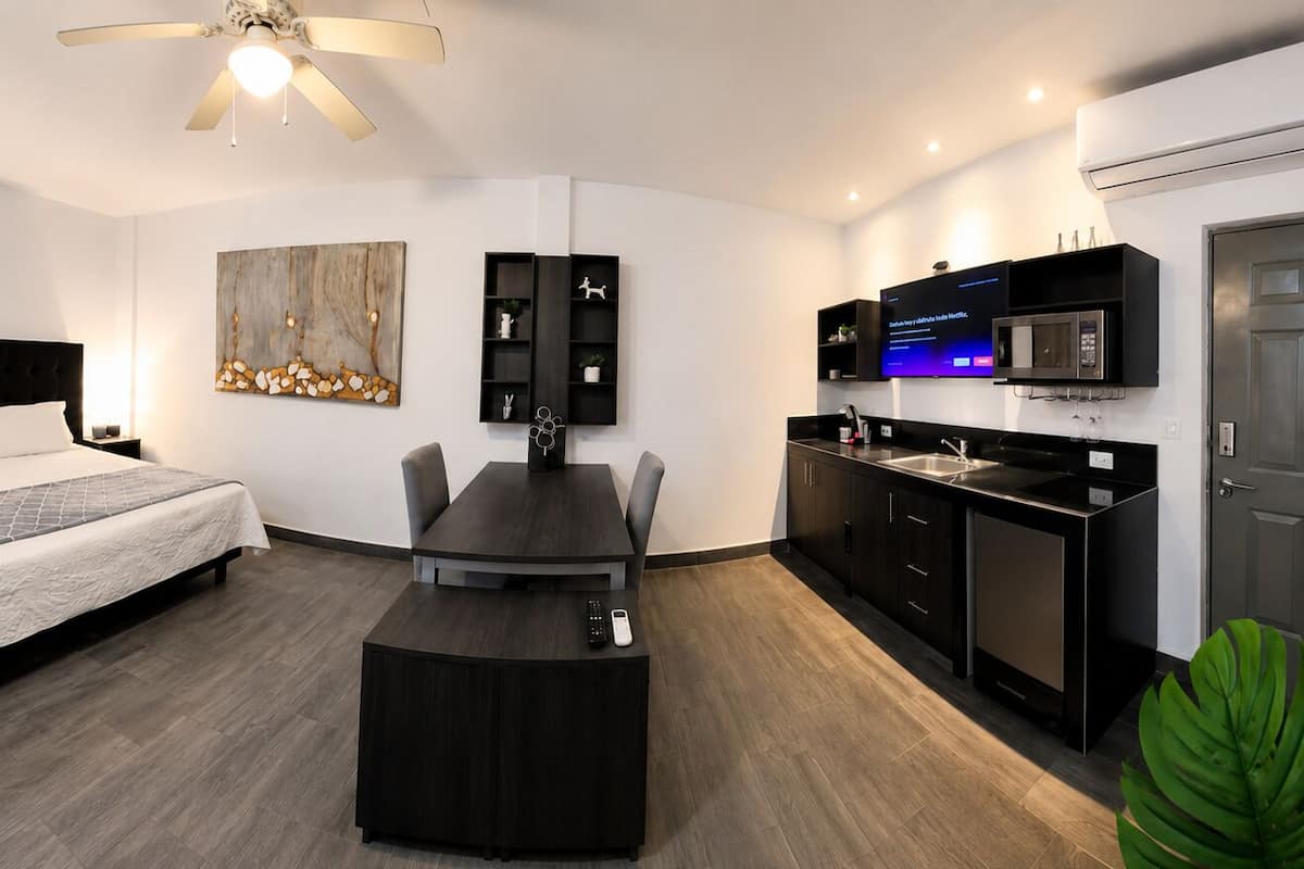 A modern hotel room with a bed, a desk, a television, and a kitchenette.