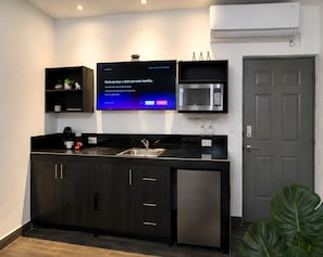 Uma cozinha moderna com micro-ondas integrado, máquina de café e televisão de tela plana exibindo a interface da Netflix.