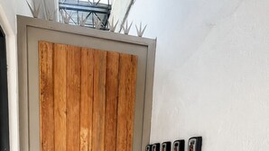 A door with a wooden panel, a black doorbell, a doormat, and a wall-mounted light fixture. - Barrio Inn Morelos (Monterrey)