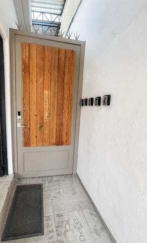 Uma porta com painel de madeira, um toque de campainha preto, um tapete de entrada e uma luminária fixada na parede.