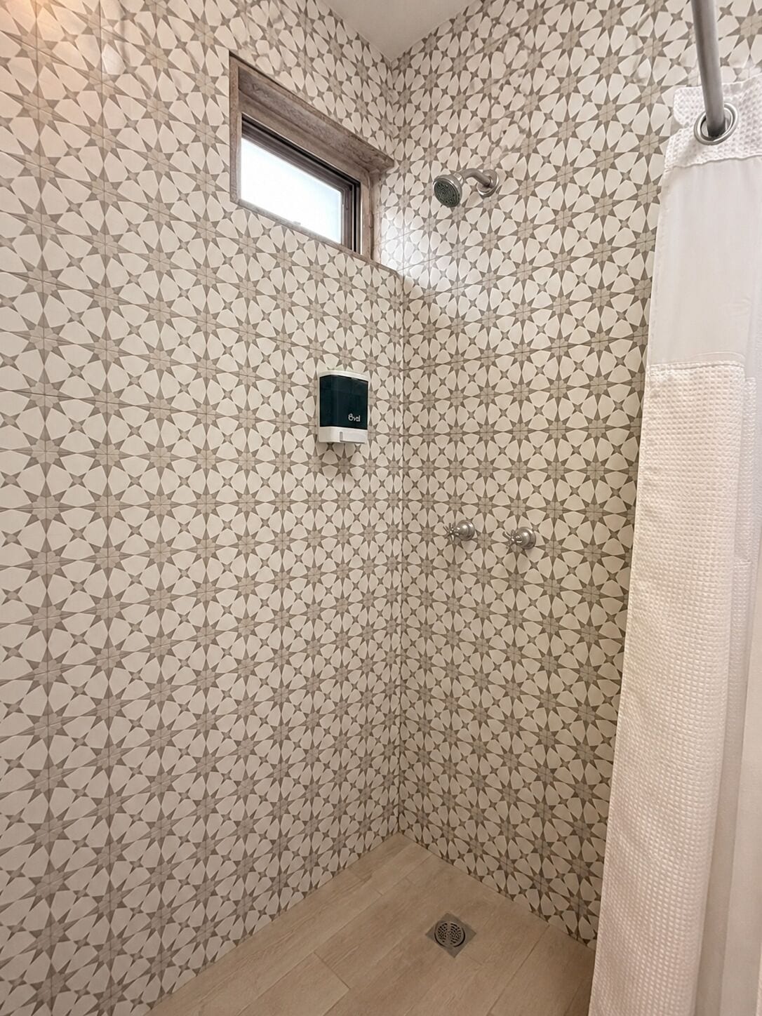 Ducha con pared de diseño geométrico, una ventana pequeña y un cabezal de ducha.