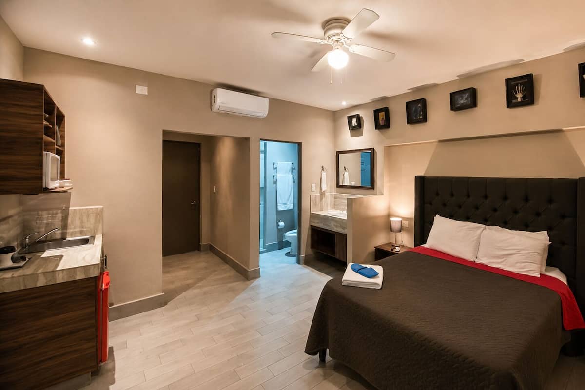 A hotel room with a bed, a desk, a bathroom, and a ceiling fan.