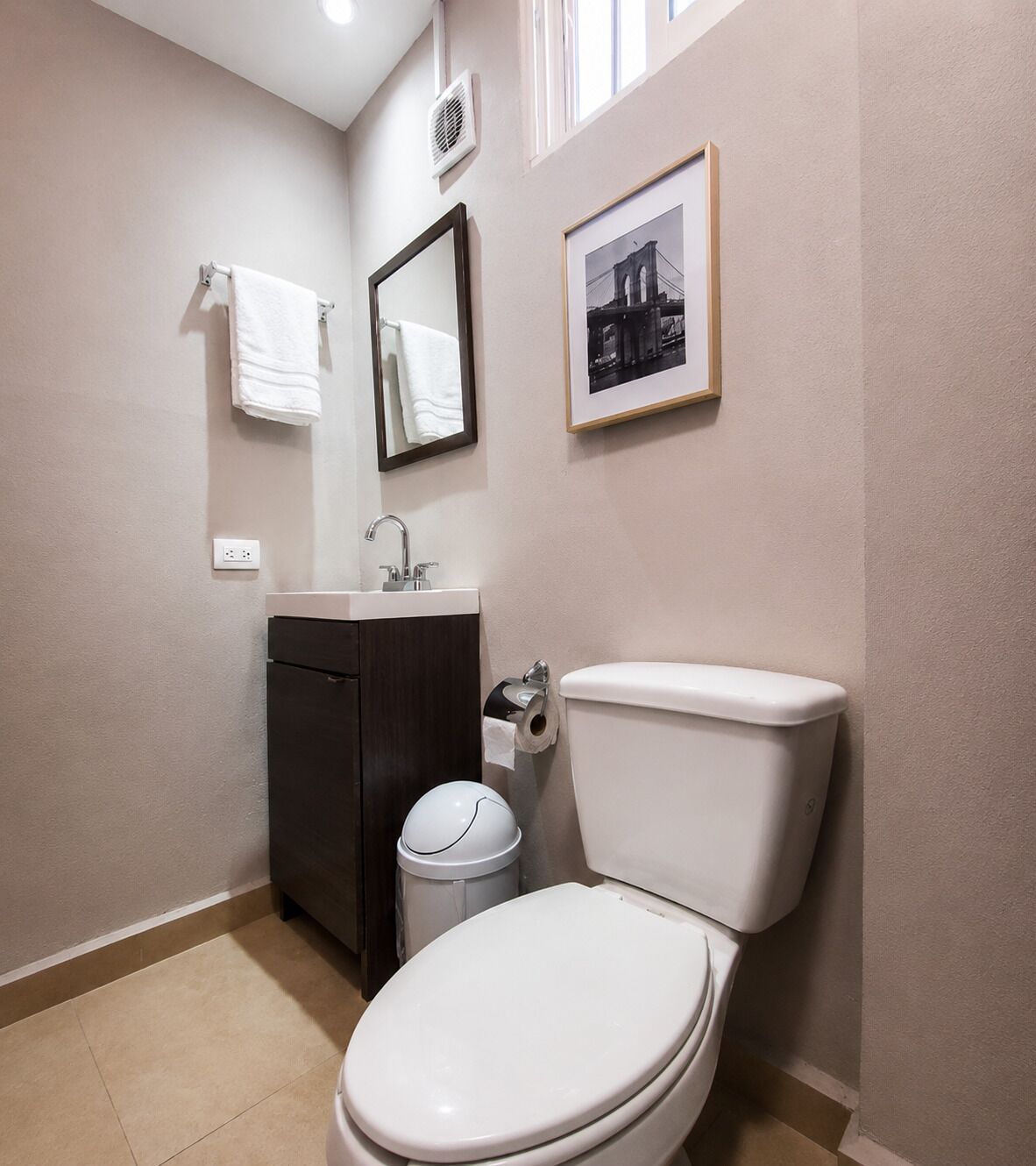A bathroom with a toilet, sink, mirror, and a framed picture on the wall.