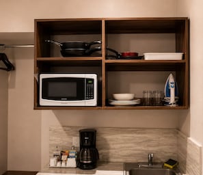 A kitchen with a microwave, coffee maker, and shelves containing cookware and dishes.