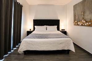 Cama bem arrumada com cabeceira acolchoada, duas mesas de cabeceira com luminárias e uma obra de arte na parede.