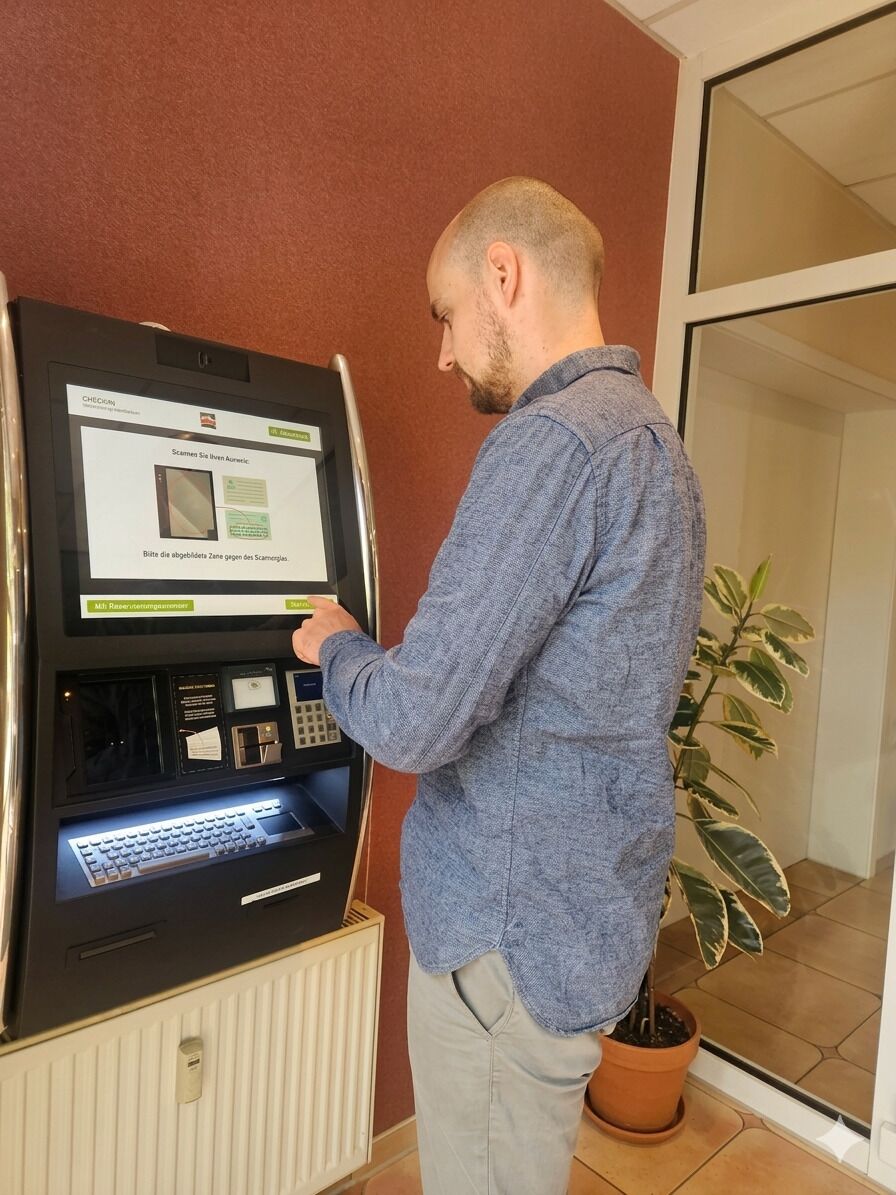 Un hombre interactuando con un quiosco de autoservicio, posiblemente para registrarse en un hotel u obtener información.
