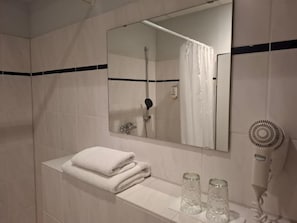 A bathroom with a white sink, a mirror, a towel rack, a shower, and a hairdryer.