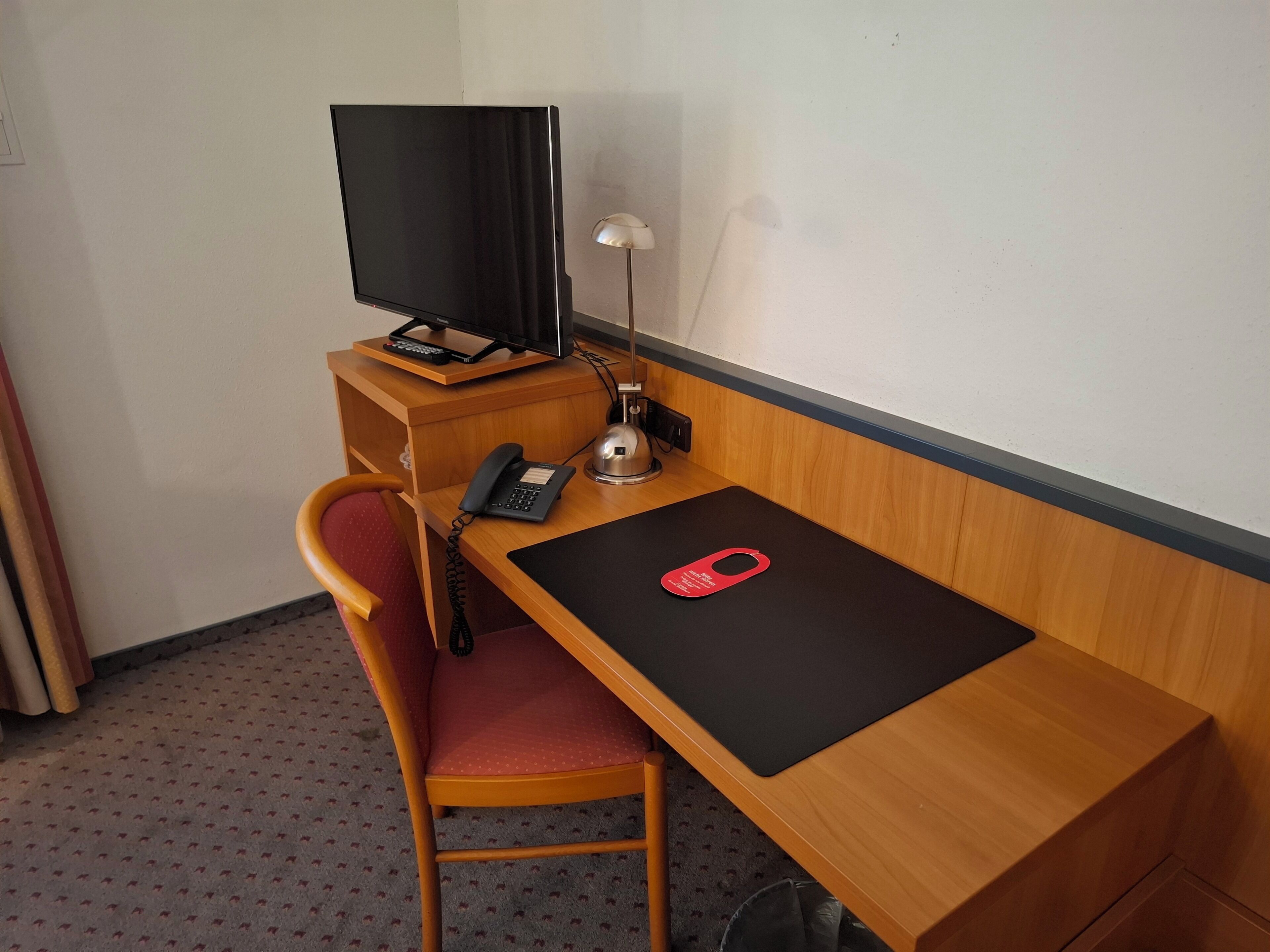 Une chambre d’hôtel avec un bureau en bois, une télévision, une lampe de bureau, un téléphone et un porte-clés rouge posé sur le bureau.
