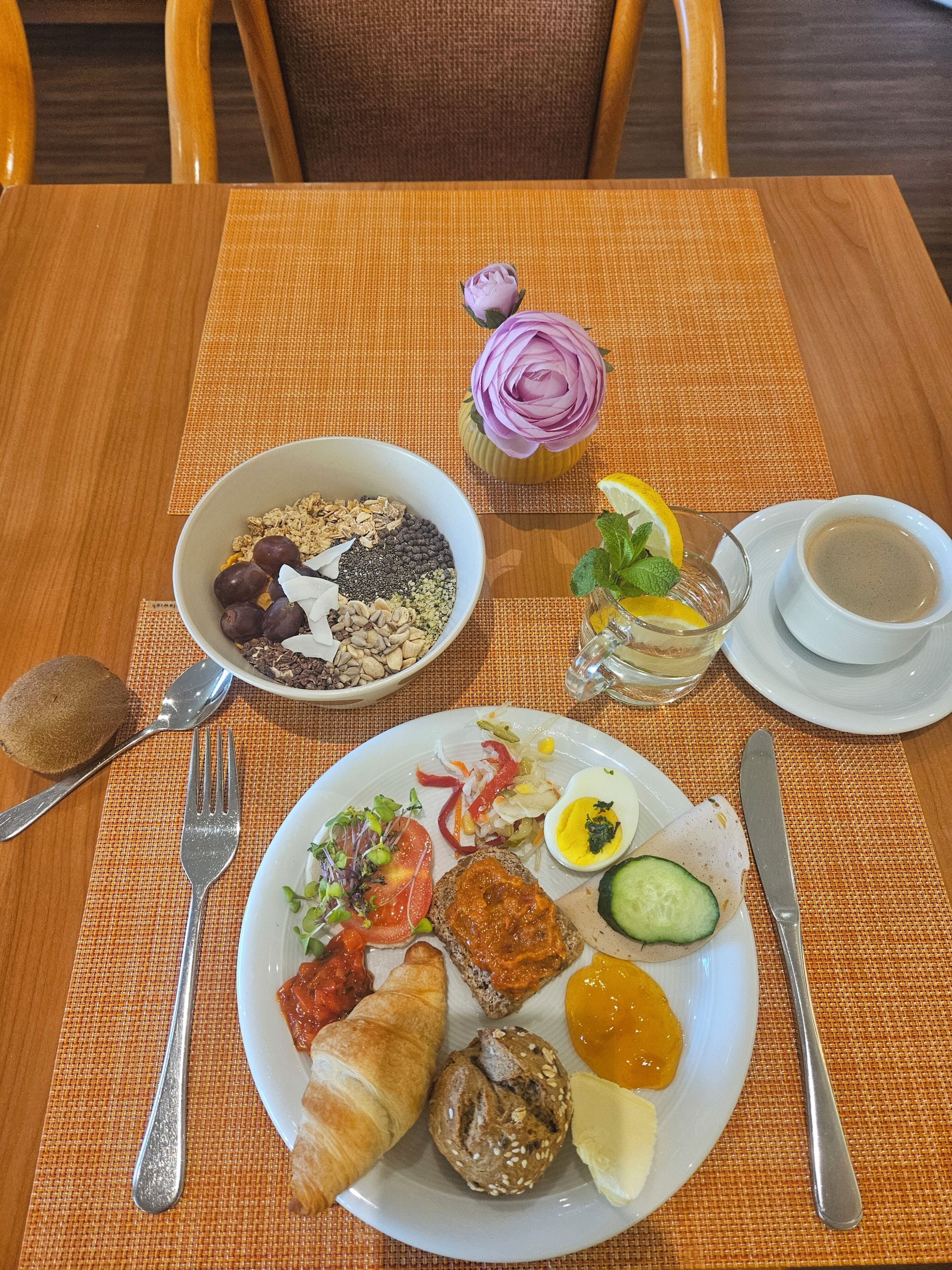 A breakfast setting with a plate of food, a bowl, a cup of coffee, and a rose.