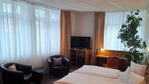 Habitación de hotel con una cama, dos sillones, un televisor, un escritorio y una planta.