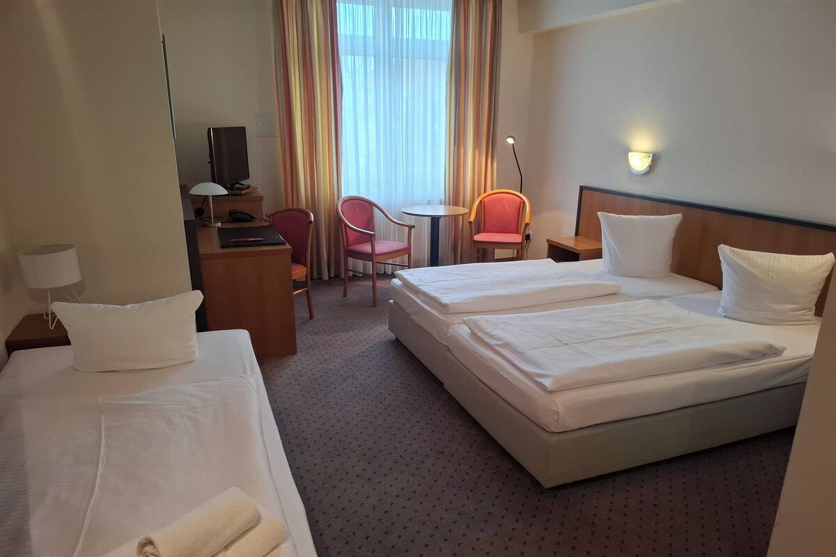 Une chambre d’hôtel avec deux lits, un bureau, une chaise, une lampe et une vue sur l’extérieur.