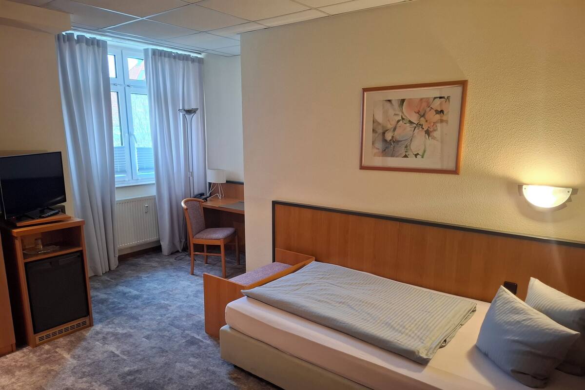 Une chambre d’hôtel avec un lit, un bureau, une chaise, une télévision et un tableau au mur.