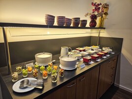 Montaje de bufé con diversos alimentos, una olla grande de sopa y un jarrón con flores en la barra.