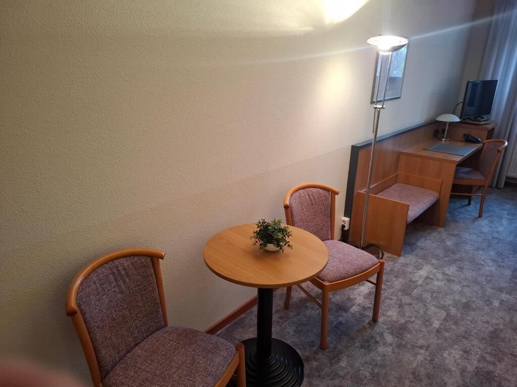A small room with a round table, two chairs, a desk, a lamp, and a television.