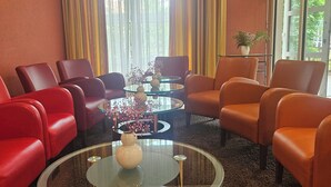 Una habitación con sillas rojas y naranjas, una mesa de centro de vidrio y vistas amplias por grandes ventanales.