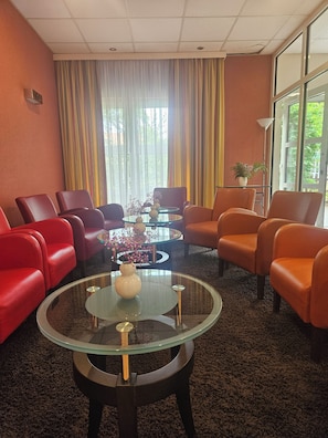 Una habitación con sillas rojas y naranjas, una mesa de centro de vidrio y vistas amplias por grandes ventanales.