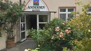 Entrada de un hotel con un letrero, un camino y follaje circundante.