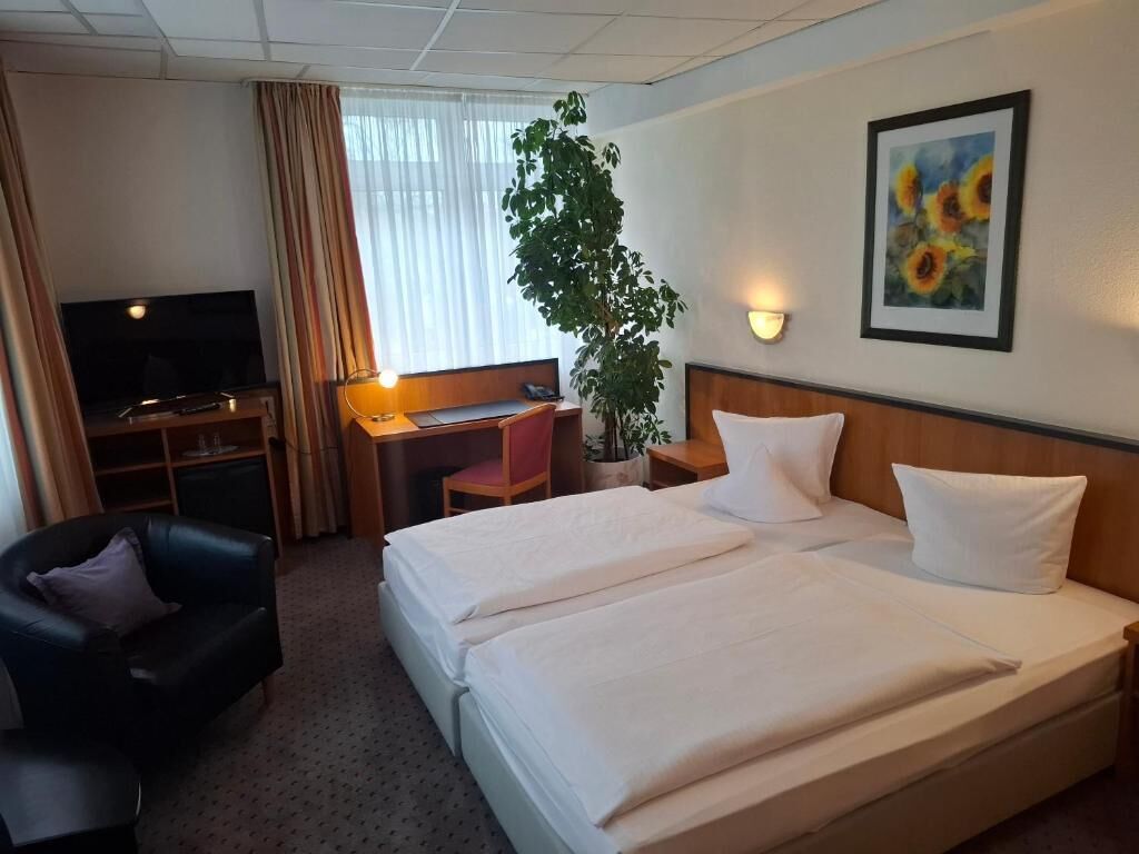 Ein Hotelzimmer mit Bett, Schreibtisch, Stuhl, Fernseher und einem Gemälde.
