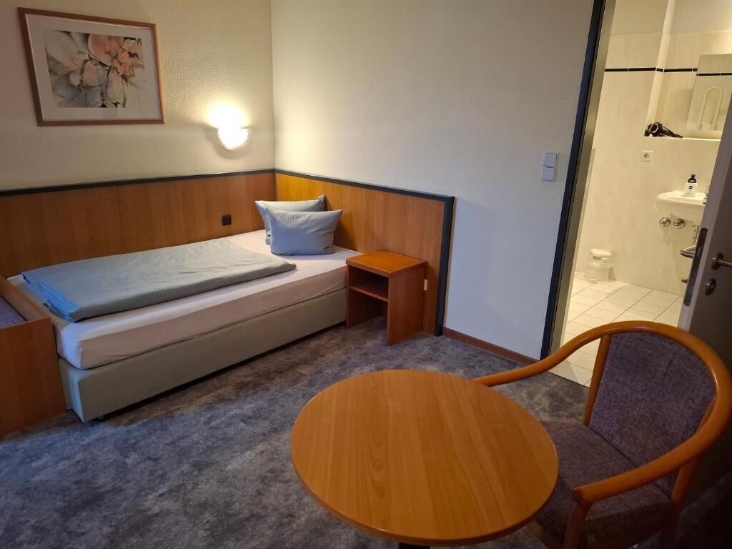 Ein kleines Zimmer mit einem Bett, einem Nachttisch, einem Stuhl und einer Dusche.